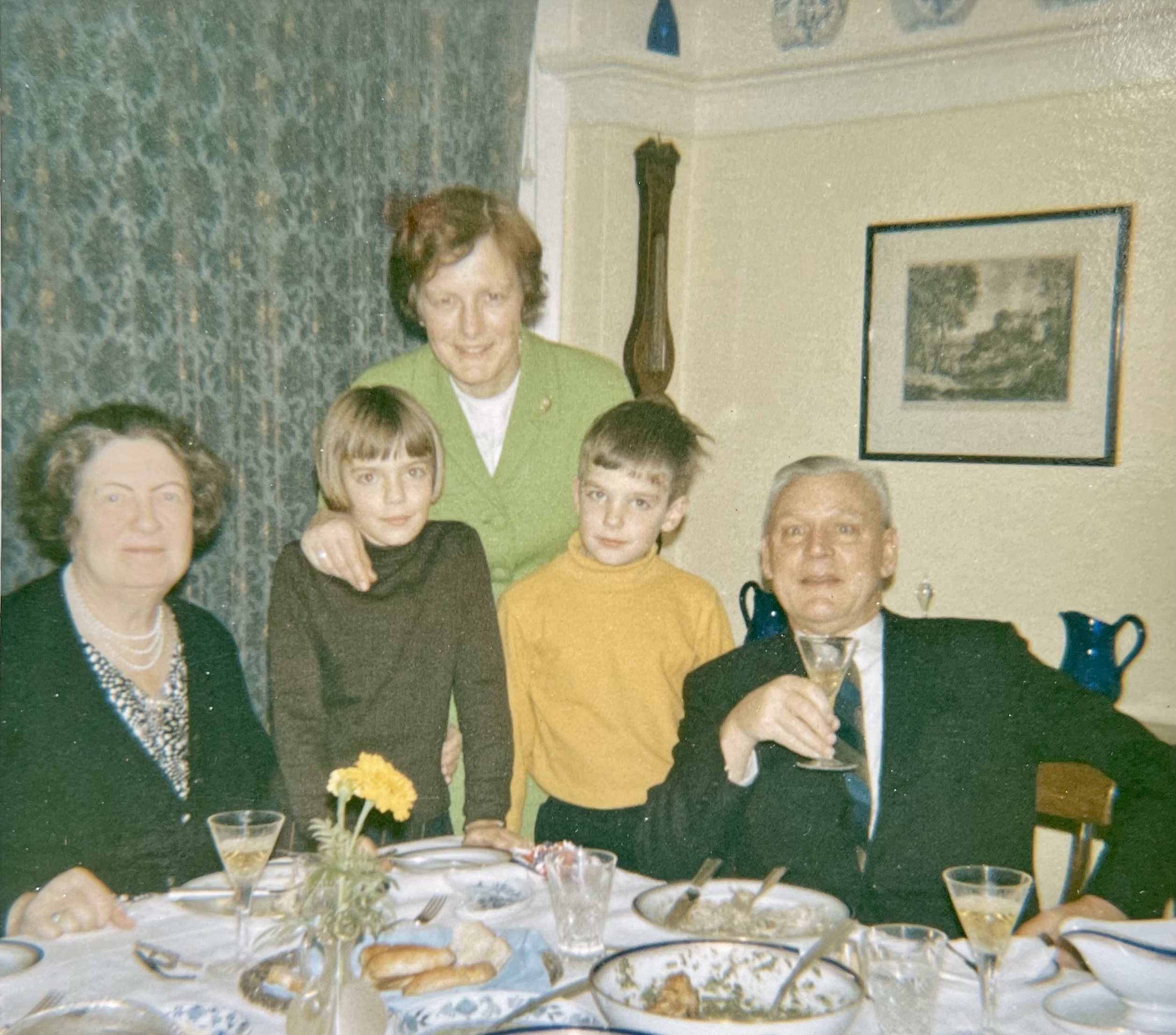 Photograph with three adults, two children, a table set with food in foreground. 